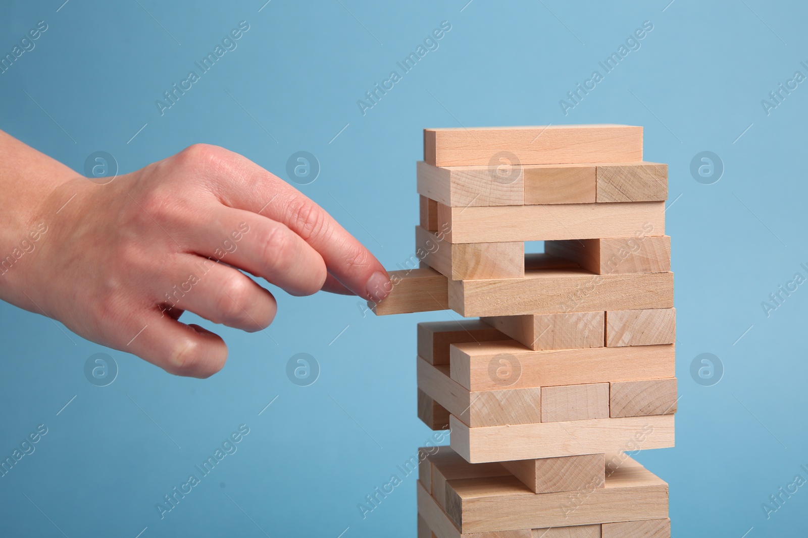 Photo of Woman playing Jenga on light blue background, closeup