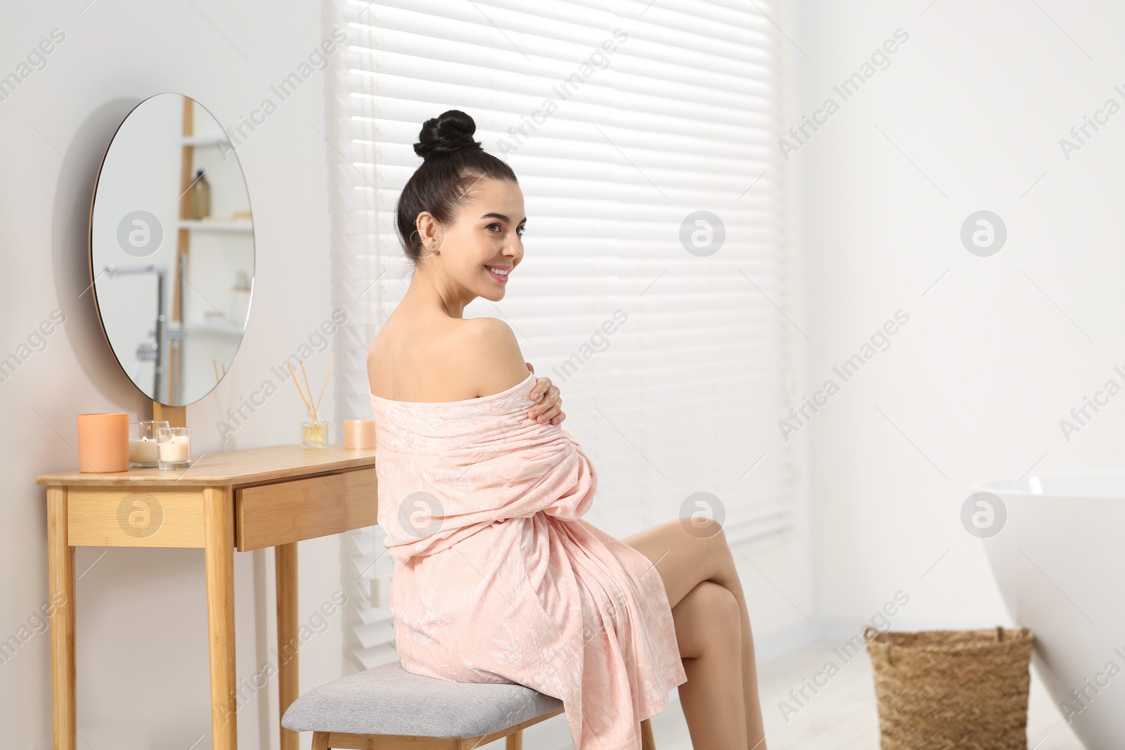 Photo of Beautiful happy woman in stylish bathrobe sitting on bench in bathroom