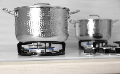 Photo of Shiny steel saucepans on modern gas stove, closeup