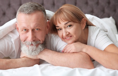 Mature couple together under blanket in bed at home