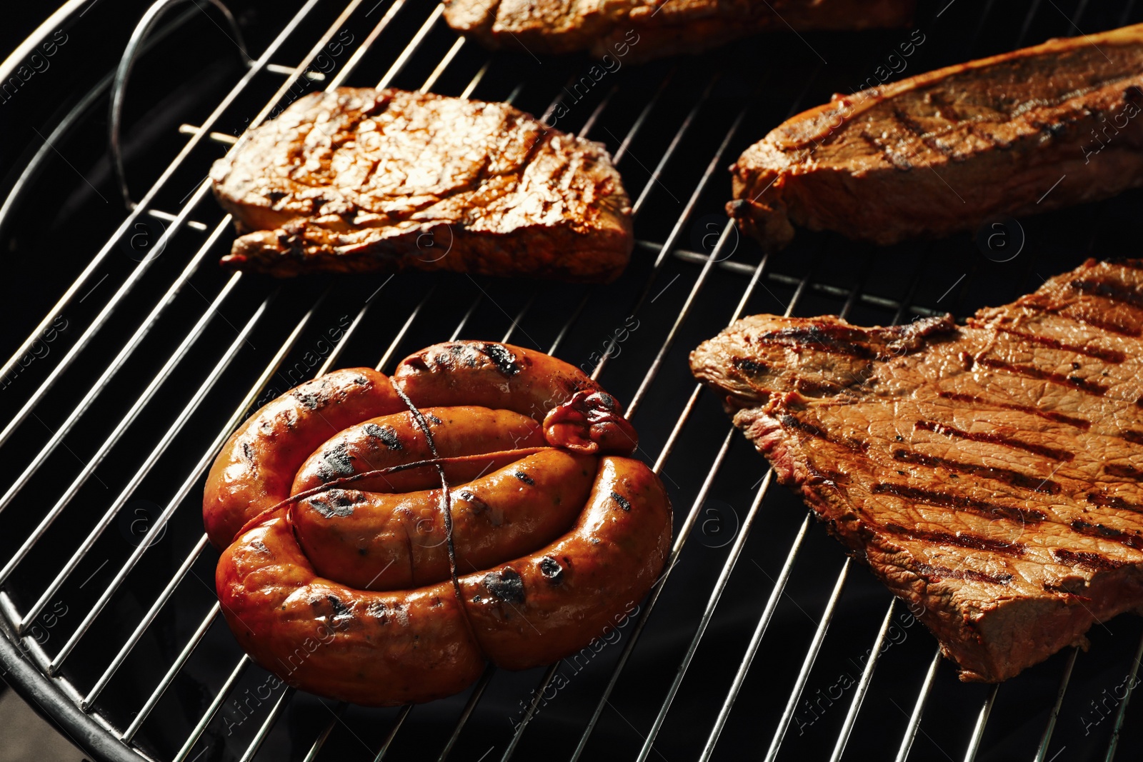 Photo of Fresh grilled tasty meat steaks and sausage on barbecue grate