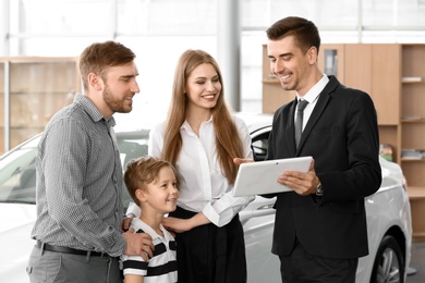 Photo of Salesman with tablet and young family in car salon