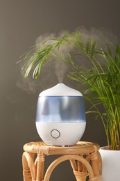 Photo of Air humidifier on wicker table near green houseplant against grey wall