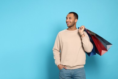 Photo of Happy African American man with shopping bags on light blue background. Space for text
