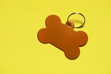 Golden pet tag in shape of bone with ring on yellow background, top view. Space for text