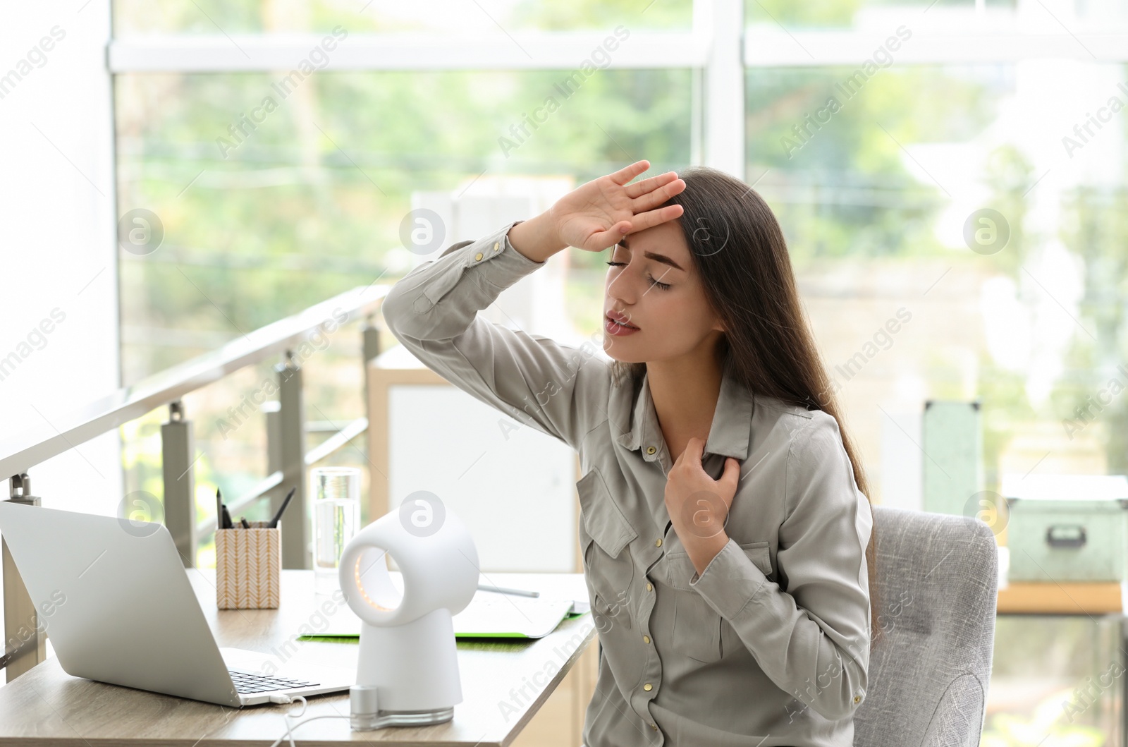 Photo of Young woman with portable fan suffering from heat at workplace. Summer season