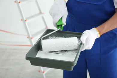 Photo of Man holding paint roller and tray in room, closeup