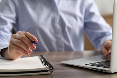 Photo of E-learning. Woman using laptop during online lesson at table indoors, closeup