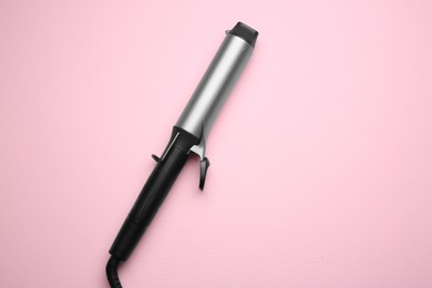 Photo of Hair styling appliance. One curling iron on pink background, top view with space for text