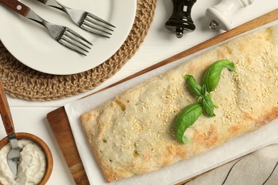 Delicious strudel with tasty filling and basil served on white wooden table, flat lay