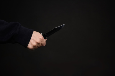 Man holding knife on black background, closeup with space for text. Dangerous criminal