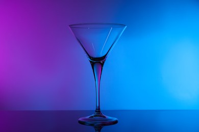Photo of Empty clean martini glass on mirror table in neon lights
