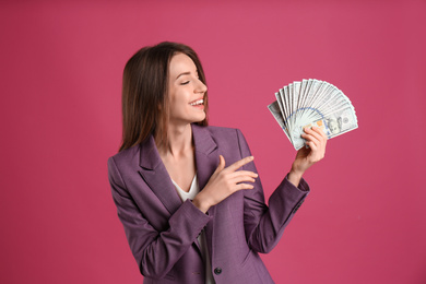 Happy young woman with cash money on pink background