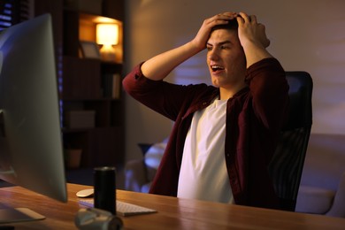 Photo of Emotional man playing video games on computer at table indoors