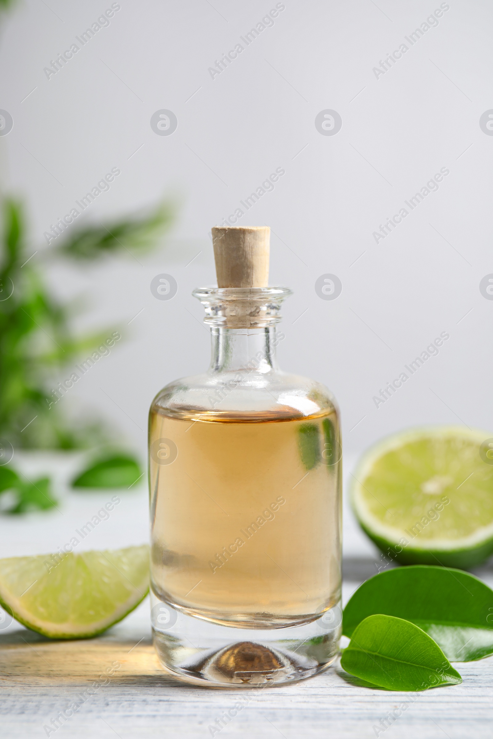 Photo of Lime essential oil and cut citrus fruits on white wooden table