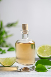 Photo of Lime essential oil and cut citrus fruits on white wooden table