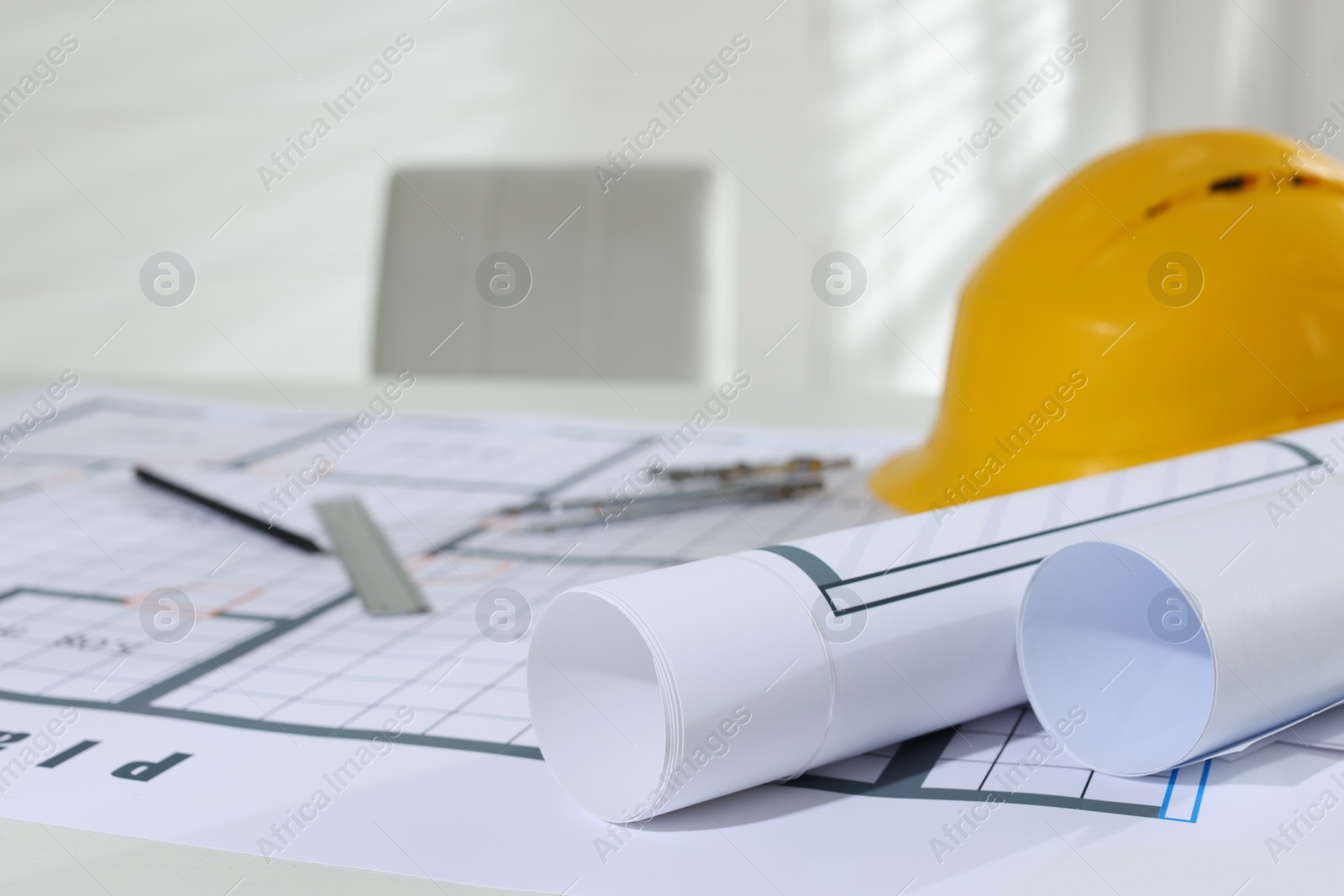 Photo of Construction drawings, safety hat and stationery on table in office