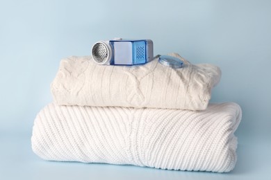 Modern fabric shaver and knitted clothes on light blue background