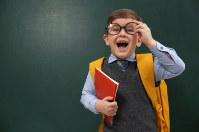 Photo of Funny little child wearing glasses near chalkboard, space for text. First time at school