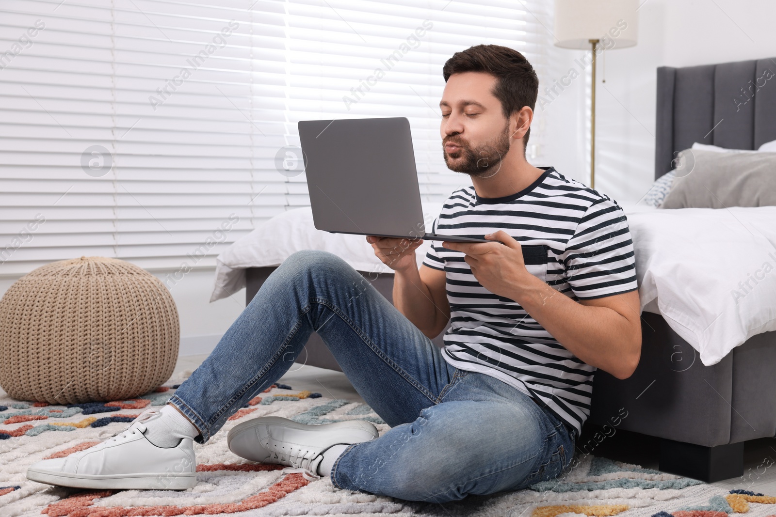 Photo of Man sending air kiss during video chat via laptop in bedroom. Long-distance relationship