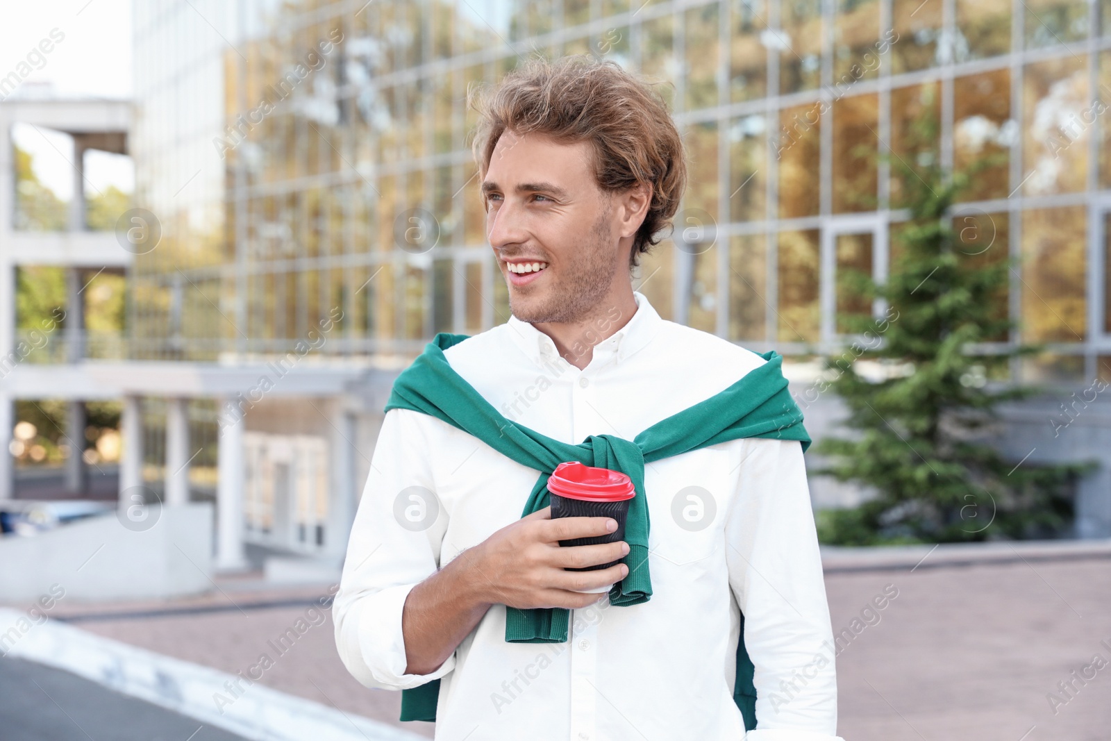 Photo of Portrait of handsome young man with cup of coffee on city street