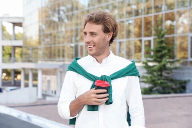 Portrait of handsome young man with cup of coffee on city street