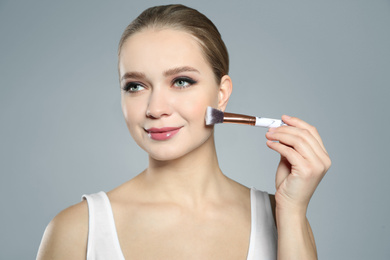 Beautiful woman applying makeup with brush on light grey background