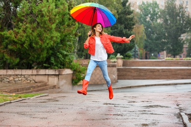 Happy young woman with bright umbrella under rain outdoors