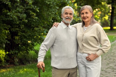 Photo of Senior man with walking cane and mature woman in park. Space for text
