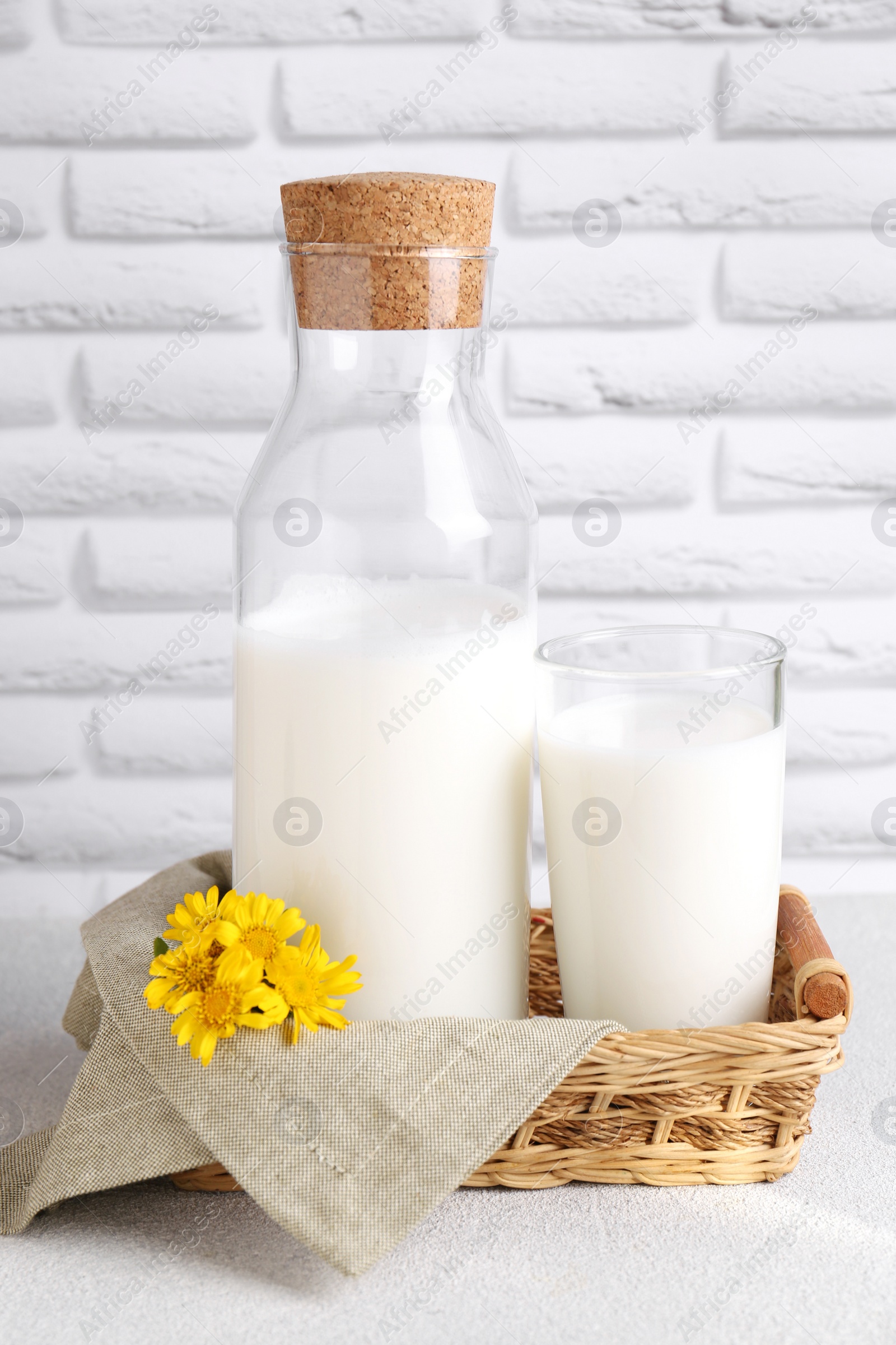 Photo of Glass and bottle of fresh milk on table against white brick wall