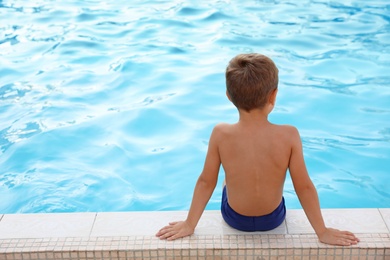 Photo of Cute little boy sitting near outdoor swimming pool