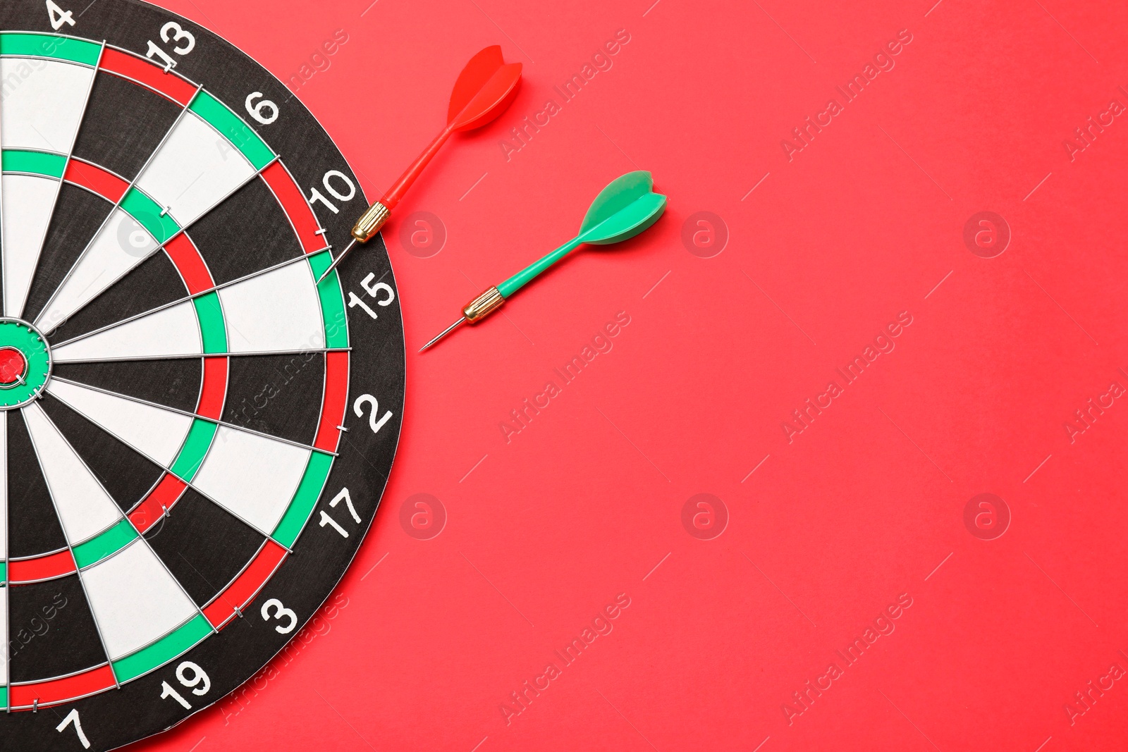 Photo of Sports equipment. Dart board with arrows on red background, top view. Space for text