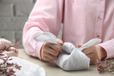 Photo of Furoshiki technique. Woman wrapping gift in white fabric at wooden table, closeup