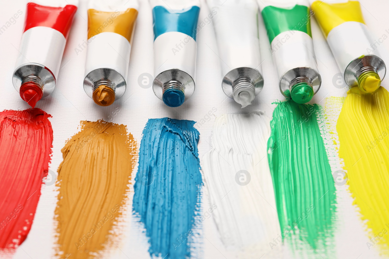 Photo of Tubes with oil paints and strokes on white canvas, closeup