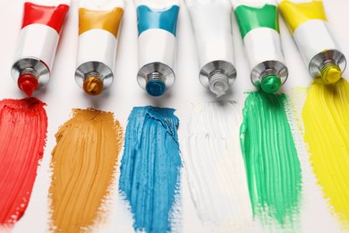 Photo of Tubes with oil paints and strokes on white canvas, closeup