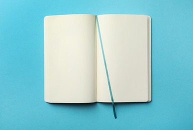 Photo of Stylish open notebook with blank sheets on light blue background, top view