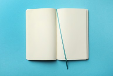 Stylish open notebook with blank sheets on light blue background, top view