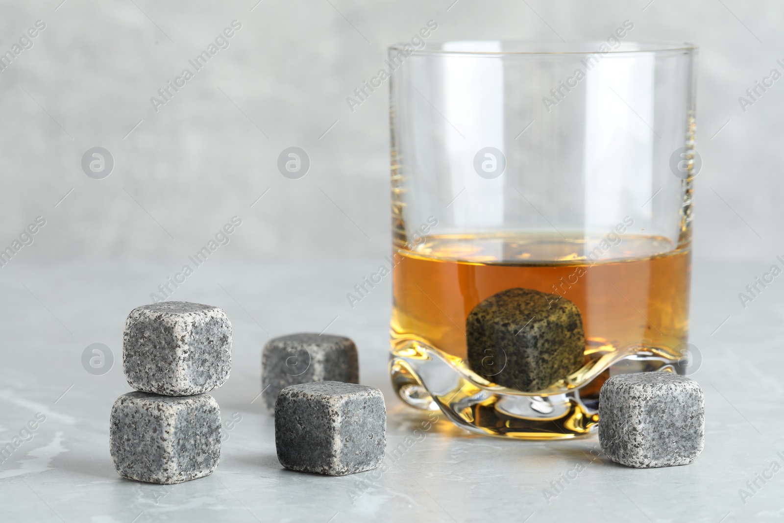 Photo of Whiskey stones and drink in glass on light marble table, closeup