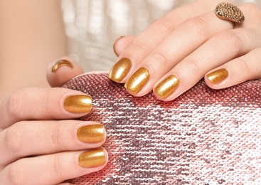 Woman holding manicured hands with golden nail polish on bag, closeup