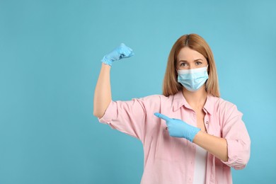 Photo of Woman with protective mask and gloves showing muscles on light blue background, space for text. Strong immunity concept