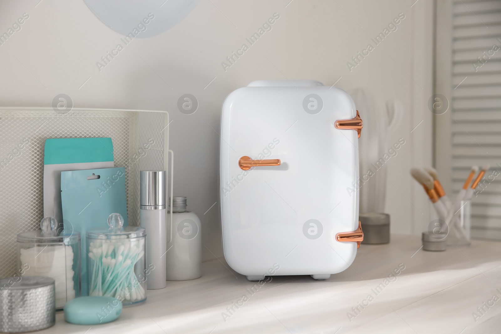 Photo of Cosmetics refrigerator and skin care products on white vanity table indoors