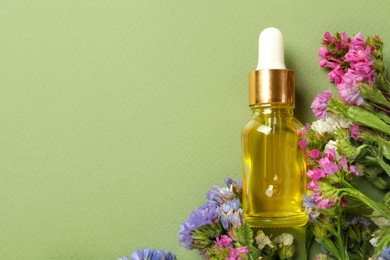 Photo of Bottle of face serum with beautiful flowers on light green background, top view. Space for text