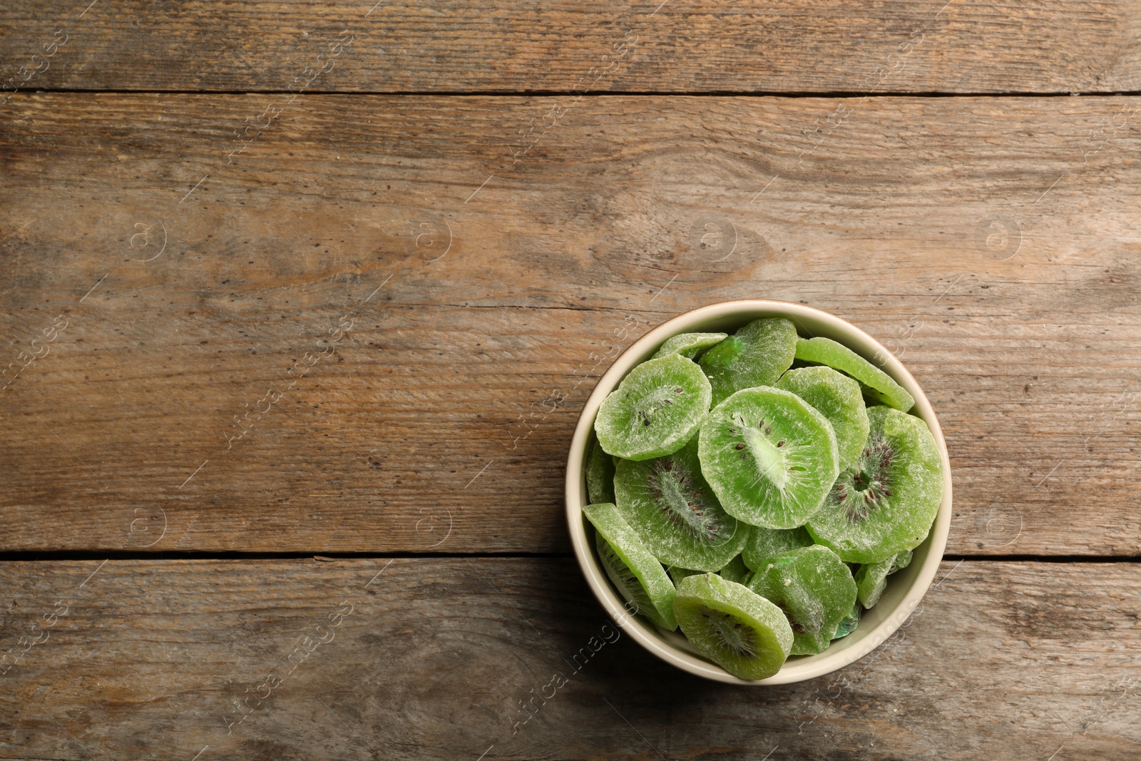 Photo of Bowl of dried kiwi on wooden background, top view with space for text. Tasty and healthy fruit