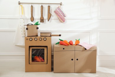 Photo of Toy cardboard kitchen with stove and utensils at home