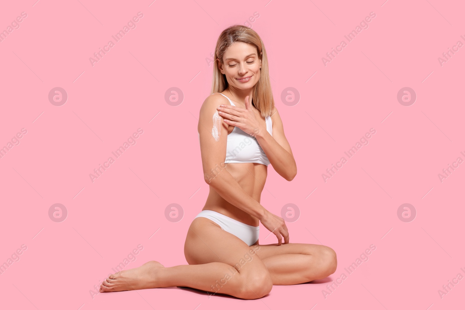 Photo of Woman applying body cream onto her arm against pink background