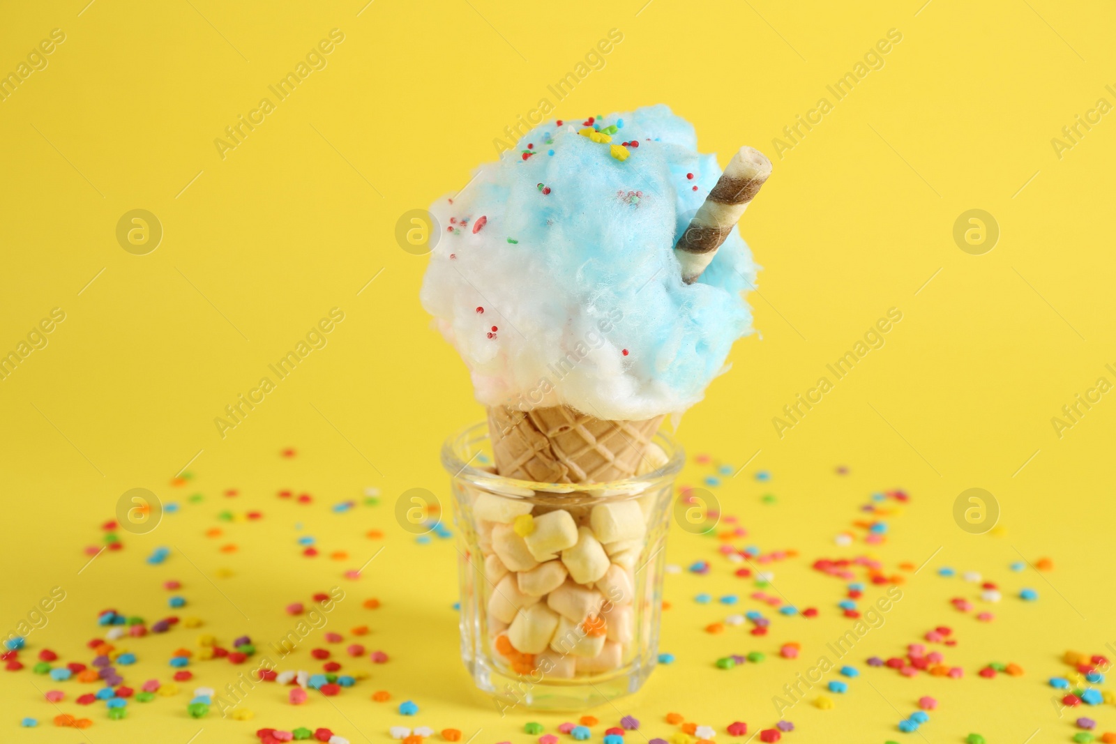 Photo of Sweet cotton candy in waffle cone on yellow background, closeup