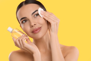 Photo of Beautiful woman removing makeup with cotton pad on yellow background. Space for text
