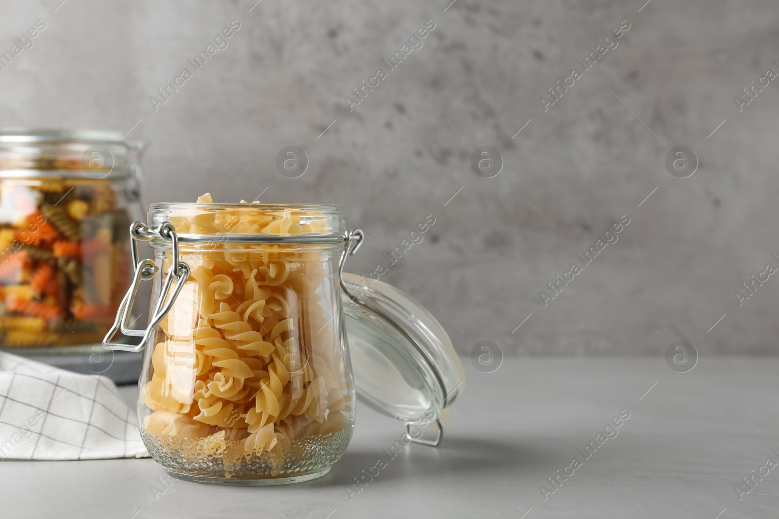 Photo of Pasta in glass jars on grey table, space for text