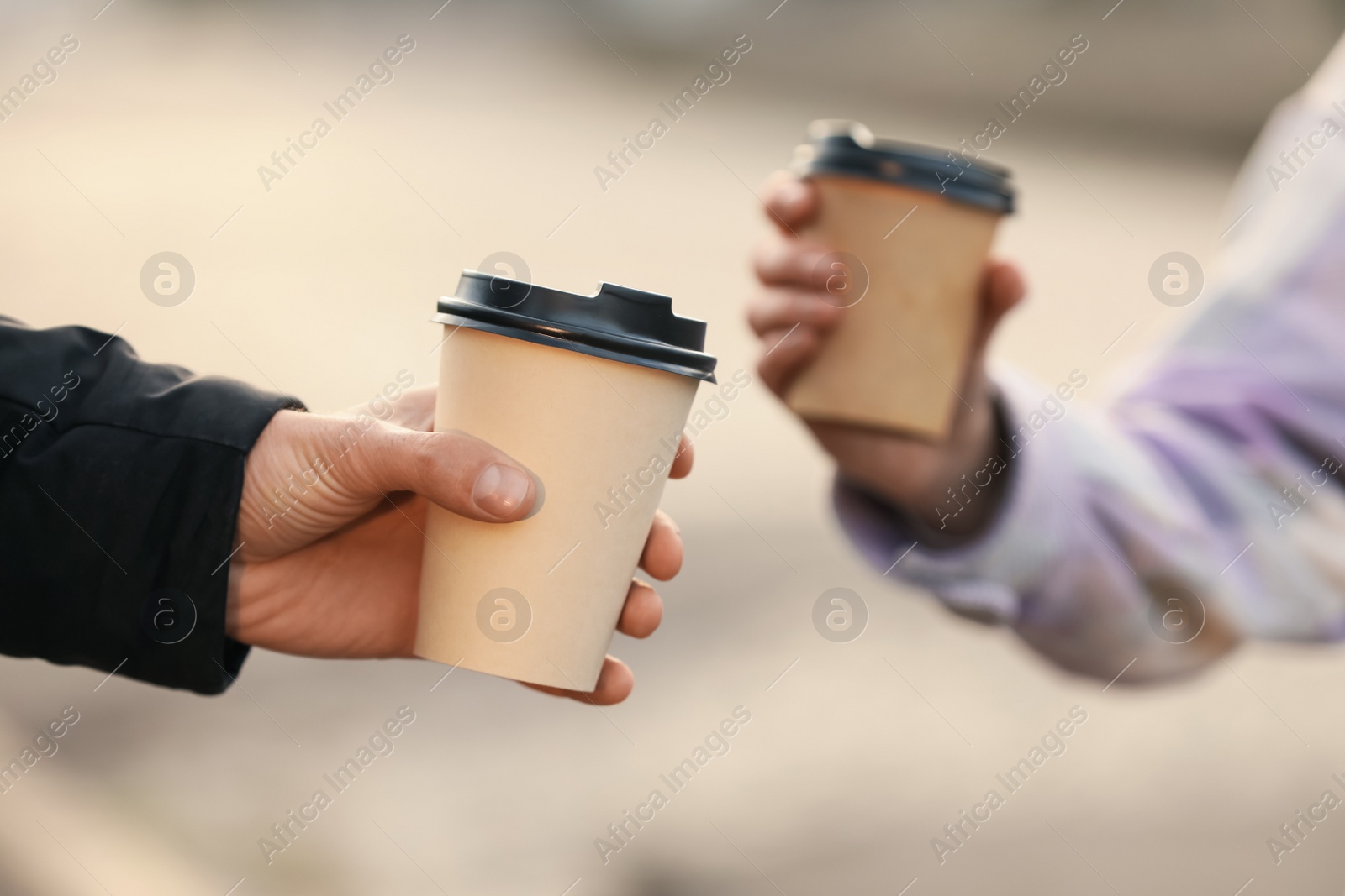 Photo of Man and woman holding paper coffee cups on blurred background, closeup