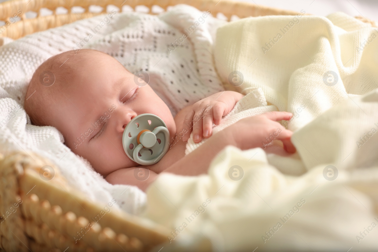 Photo of Cute newborn baby sleeping on white blanket in wicker crib, closeup